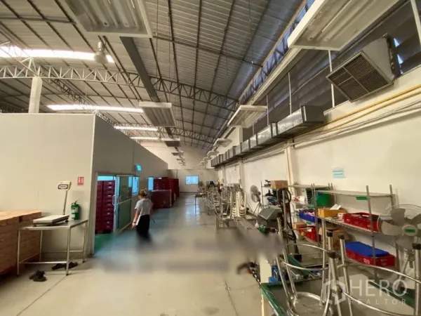 Warehouse for rent in Bueng Kum, Bangkok - Long aisle with ventilation ducts, stainless shelving, and workstations beneath a metal roof.