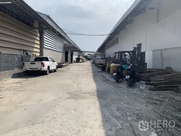 Warehouse for rent in Bueng Kum, Bangkok - Warehouse complex driveway in Bueng Kum, Bangkok with trucks, forklifts and loading materials along both sides.