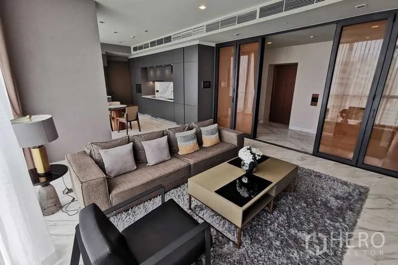 Condominium for rent or sale in Watthana, Bangkok - Bright living room with floor-to-ceiling windows, gray sofa and coffee table on a rug.