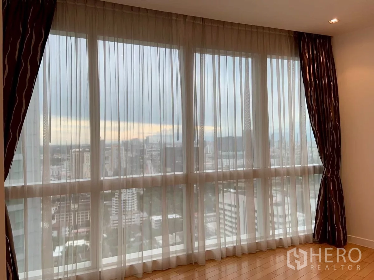 Condominium for rent in Khlong Toei, Bangkok - City skyline through full-height windows from a high floor.