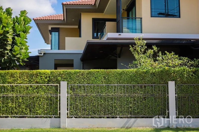 Detached House for rent or sale in Lam Luk Ka, Pathum Thani - Side exterior view showing balcony, eaves and manicured hedges.