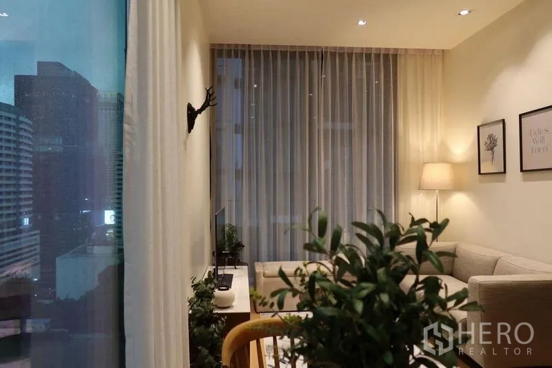Condominium for rent in Pathum Wan, Bangkok - View from dining toward the living area and window with dusk city skyline and warm lighting.