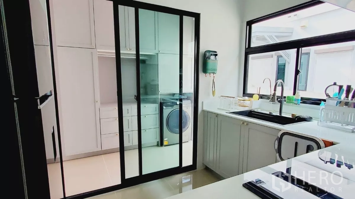 Detached House for rent in Lat Krabang, Bangkok - Kitchen linked to laundry through black-framed sliding glass doors and a large sink.