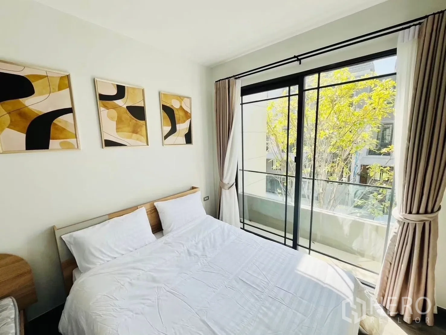 联排别墅 for rent in Suan Luang, Bangkok - 明亮卧室配双人床与墙面装饰，推拉门通向绿意阳台。