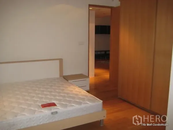 Condominium for rent or sale in Sathon, Bangkok - Bedroom with bed frame, bedside table and large wardrobe on warm hardwood flooring.