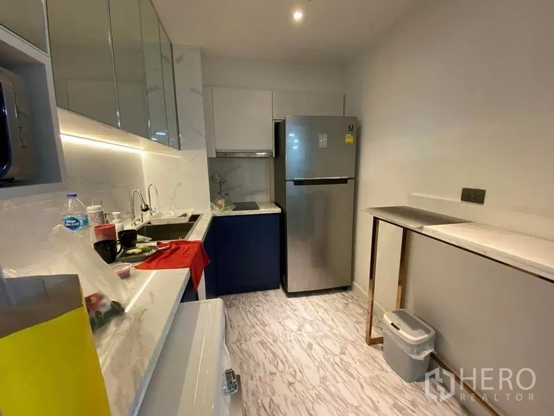 Condominium for sale in Huai Khwang, Bangkok - Modern galley kitchen with glossy cabinets, under-cabinet lighting, marble-look surfaces and a stainless refrigerator.