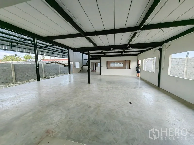 Factory for rent or sale in Mueang Samut Prakan, Samut Prakan - Ground-floor workspace with steel columns, large windows and stair to the mezzanine.