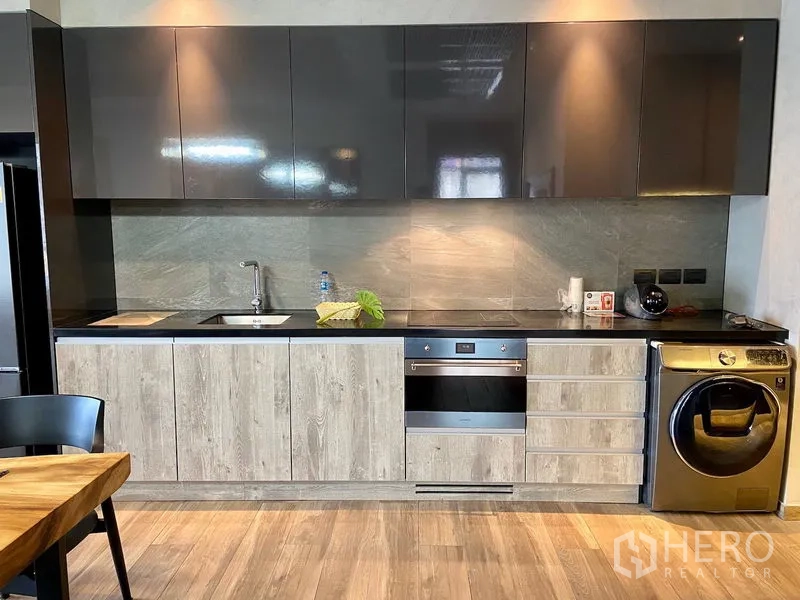 公寓 出租在Watthana, Bangkok - 一字型现代厨房，亮面吊柜、内置烤箱、水槽与洗烘一体机。