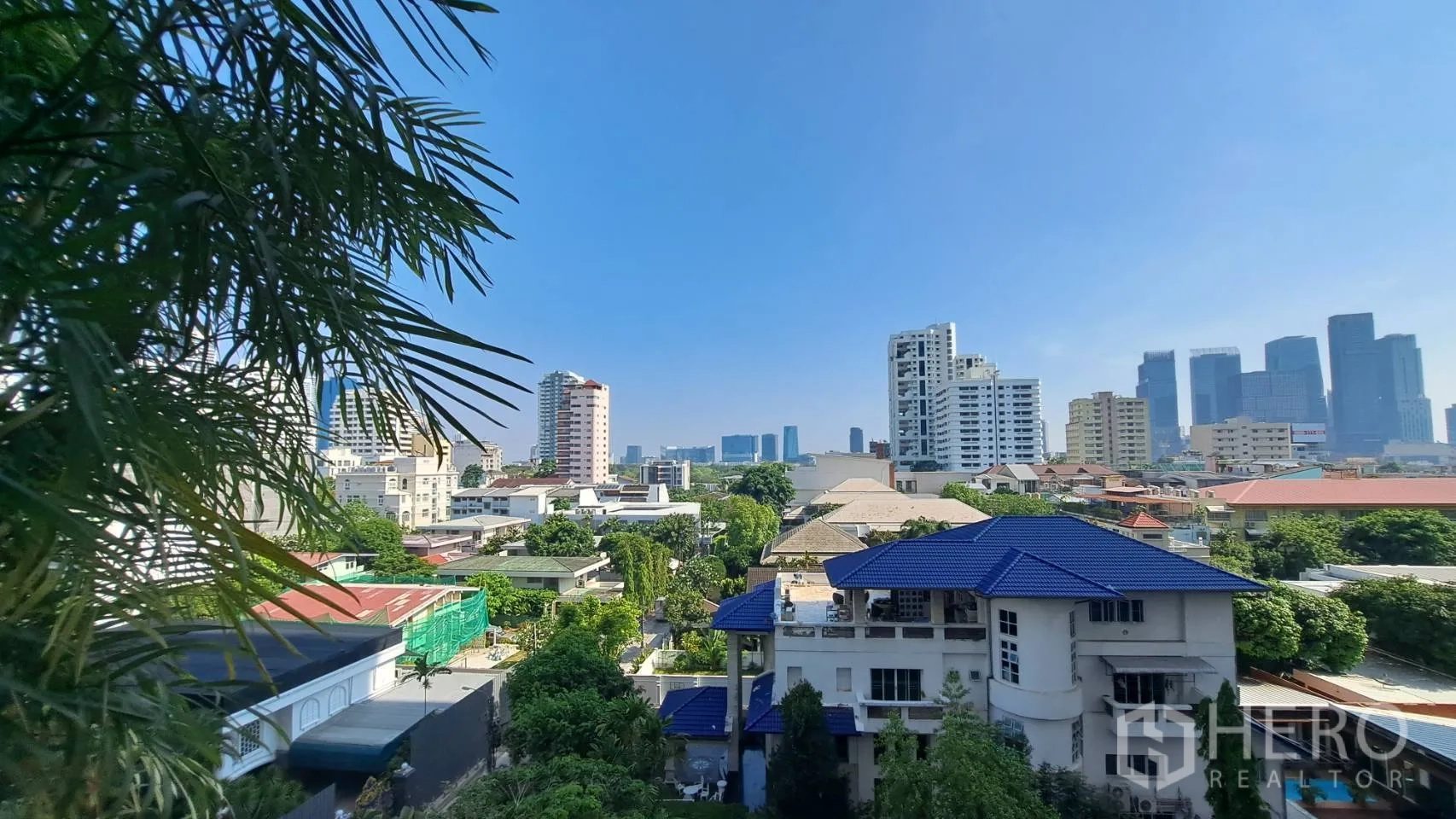 Condominium for rent in Khlong Toei, Bangkok - Balcony view of city skyline and rooftops with lush trees.