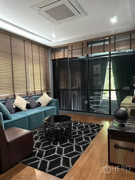 Detached House for rent in Phra Khanong, Bangkok - Family sitting area with teal sofa, patterned rug, and glass partition.