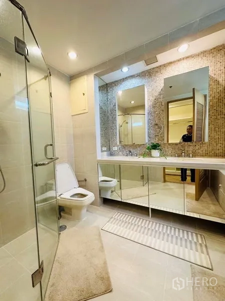 Condominium for rent in Bang Rak, Bangkok - Spacious bathroom with glass-enclosed shower, long vanity, mosaic backsplash, and mirrors.