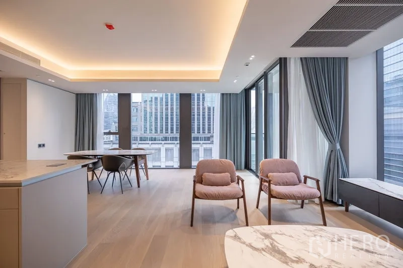 Condominium for rent in Pathum Wan, Bangkok - Open-plan space with armchairs, large windows and a cityscape backdrop.