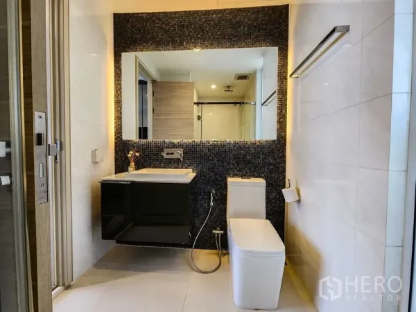 Condominium for rent or sale in Bang Rak, Bangkok - Modern bathroom with a large mirror, mosaic accent wall, and floating vanity.
