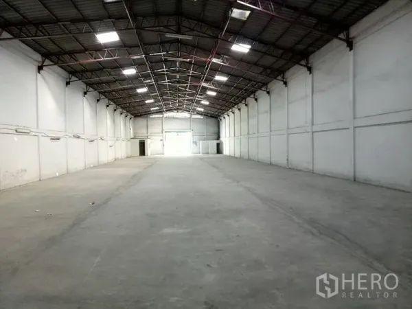 Warehouse for rent in Khlong Toei, Bangkok - Long-span warehouse hall with bright lighting, concrete flooring and a loading door at the far end.