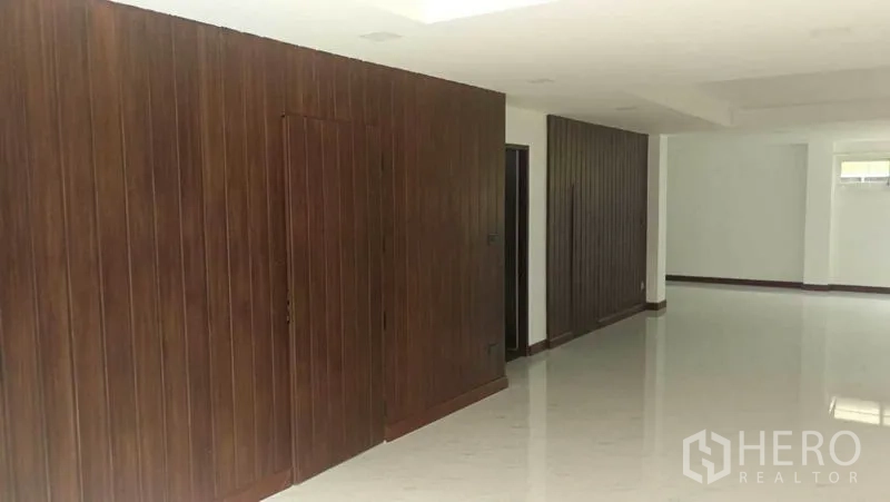 Townhouse for rent in Khlong Toei, Bangkok - Long open-plan area with wood wall paneling and glossy white flooring.
