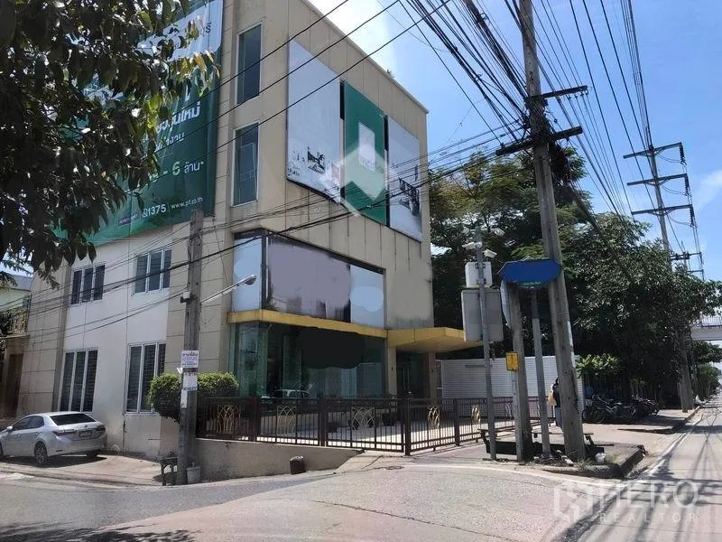 带办公室的家 出租在Min Buri, Bangkok - 转角三层商业建筑，带围栏前院与街景。