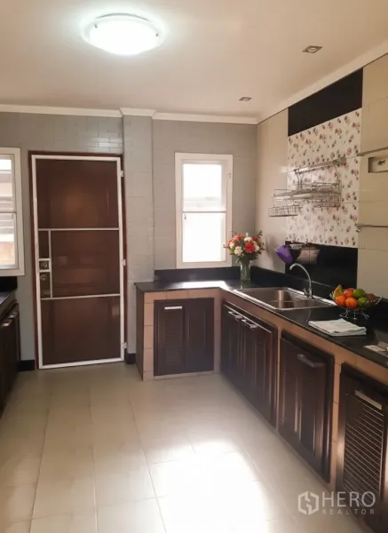 Detached House for rent in Lat Krabang, Bangkok - Bright L-shaped kitchen with dark wood cabinets, granite counters, sink and windowed back door.