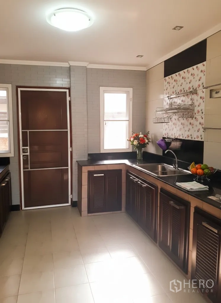 Detached House for rent in Lat Krabang, Bangkok - Bright L-shaped kitchen with dark wood cabinets, granite counters, sink and windowed back door.