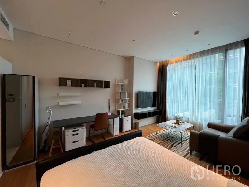 คอนโด ให้เช่าในPathum Wan, Bangkok - สตูดิโอสว่างขนาด 40 ตร.ม. มีเตียง โต๊ะทำงาน โซฟา ผนังทีวี พื้นไม้ และหน้าต่างสูงจรดเพดานพร้อมม่านโปร่ง