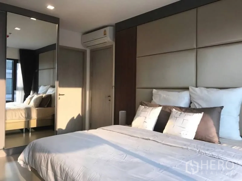 Condominium for rent or sale in Khlong Toei, Bangkok - Bedroom with large mirrored wardrobe, air conditioner and soft lighting.