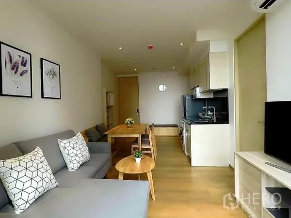 Condominium for rent in Khlong Toei, Bangkok - Bright open-plan living room with grey sofa, dining table and compact modern kitchen.