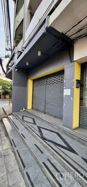 Home Office for rent in Sathon, Bangkok - Street-front facade of a shophouse-style home office with grey roller shutters, yellow pillars and tiled steps.