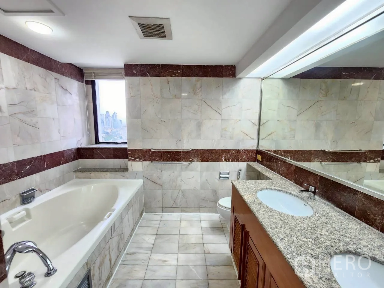 Condominium for rent in Khlong Toei, Bangkok - Spacious bathroom with long granite countertop, bathtub and window with skyline view.