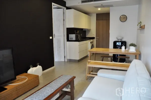 Condominium for rent in Bangkok - Open-plan lounge facing a compact white kitchen with black countertop, in-unit washer and a retro-style fridge.