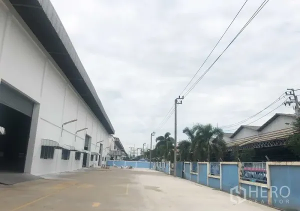 คลังสินค้า ให้เช่าในBang Sao Thong, Samut Prakan - ลานโหลดด้านข้างโกดังสีขาวกว้างขวาง พร้อมหน้าต่างหลายบานและสายไฟฟ้า