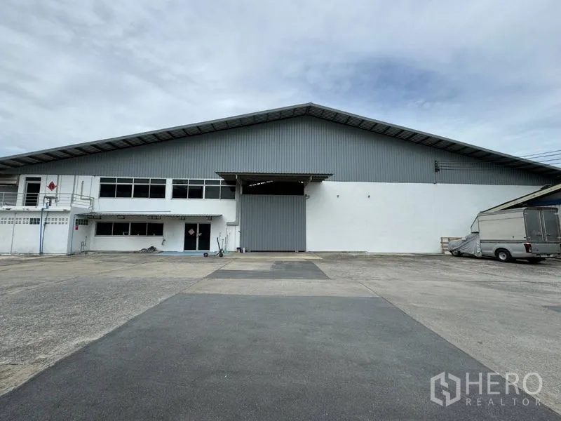 Warehouse for rent in Mueang Pathum Thani, Pathum Thani - Front view of a large warehouse with a wide roller shutter door and spacious paved truck yard.