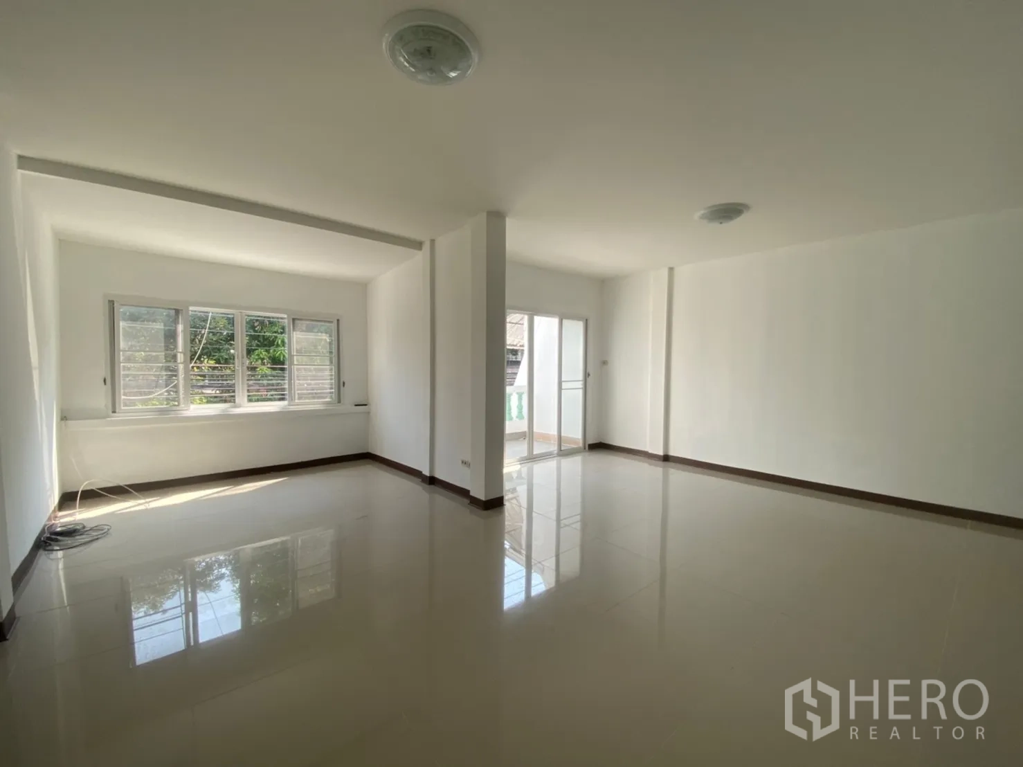Townhouse for rent in Watthana, Bangkok - Sunlit upper living space with corner windows and a door to the balcony.