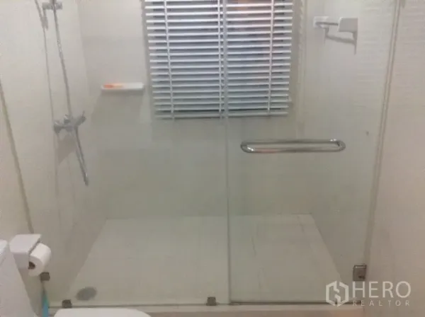 Condominium for rent or sale in Din Daeng, Bangkok - Modern bathroom with a glass-enclosed walk-in shower, white tiles, and a window blind.