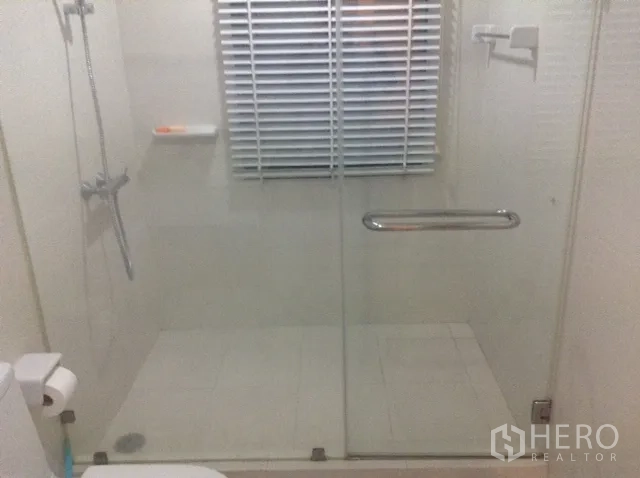 Condominium for rent or sale in Din Daeng, Bangkok - Modern bathroom with a glass-enclosed walk-in shower, white tiles, and a window blind.