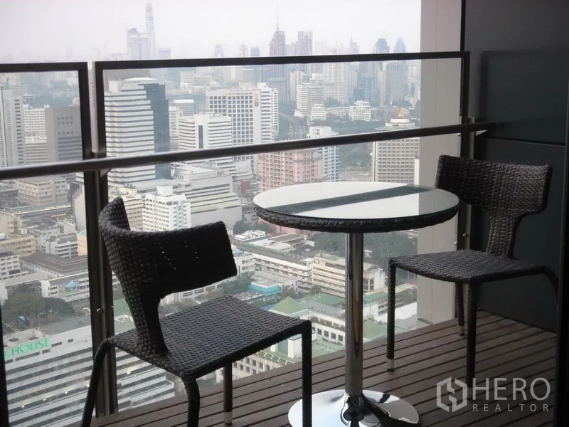Condominium for rent in Sathon, Bangkok - Balcony with two wicker chairs and round table overlooking the Bangkok skyline.