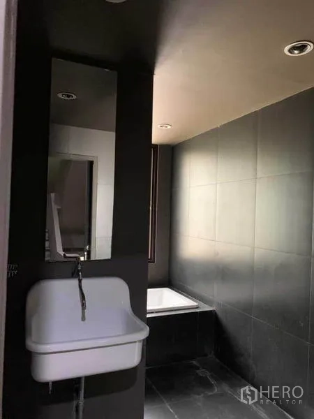 Home Office for rent in Huai Khwang, Bangkok - Dark-tiled bathroom with soaking tub and wall-mounted sink.