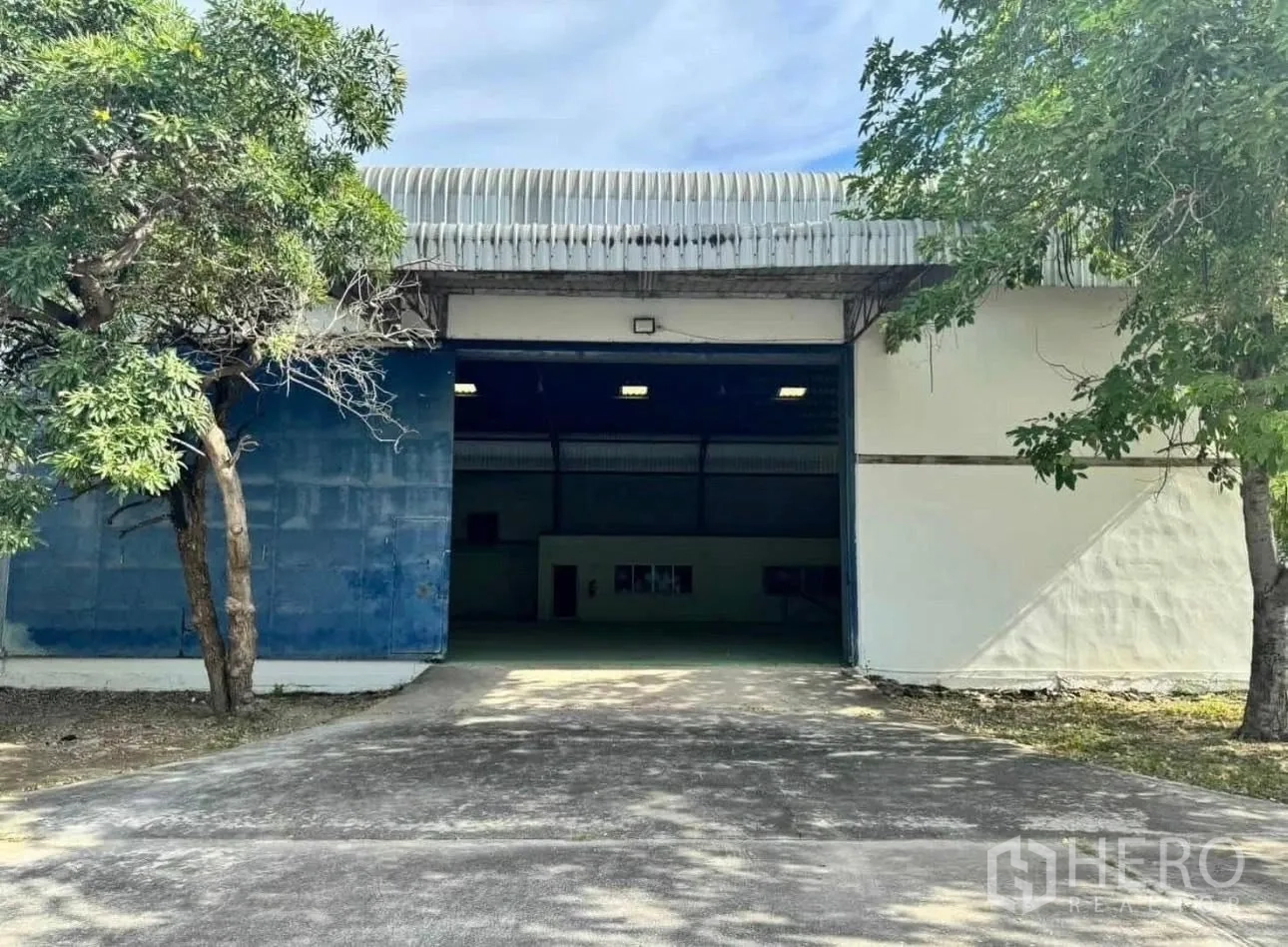 工厂 for rent in Bang Phli, Samut Prakan - 工厂外观配大型滑动门、混凝土车道与遮荫树木。