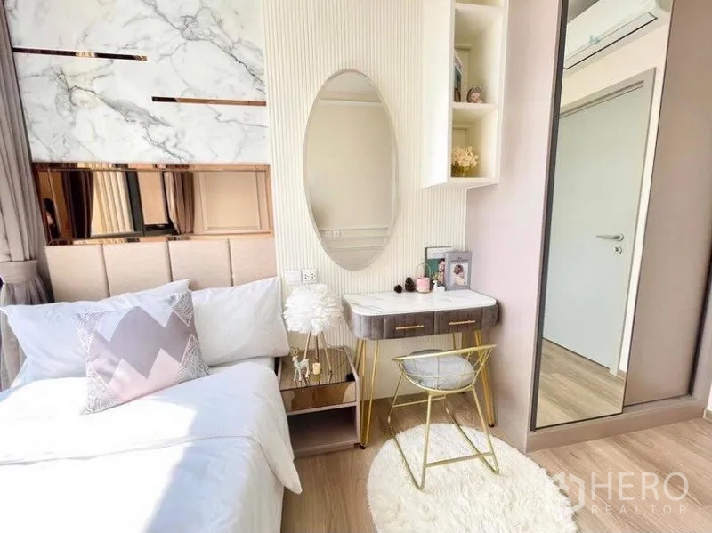 Condominium for rent in Khlong Toei, Bangkok - Cozy second bedroom with upholstered headboard, oval mirror vanity and wardrobe.