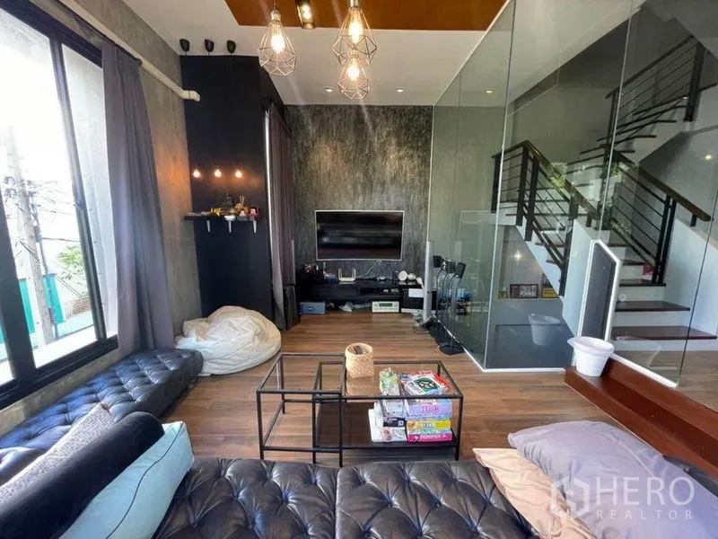 Townhouse for sale in Bang Phli, Samut Prakan - Cozy living room with TV feature wall, glass partition, staircase and leather seating.