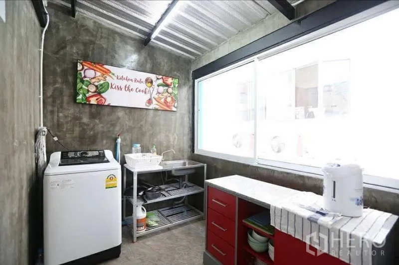 Home Office for rent in Khlong Toei, Bangkok - Compact Thai kitchen with large window, cement finish, red cabinets, and washing machine.