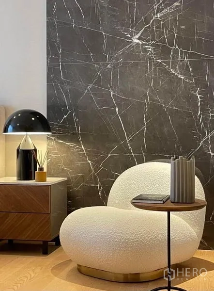 Condominium for rent or sale in Khlong Toei, Bangkok - Reading corner with sculptural white chair, nightstand, and modern table lamp.