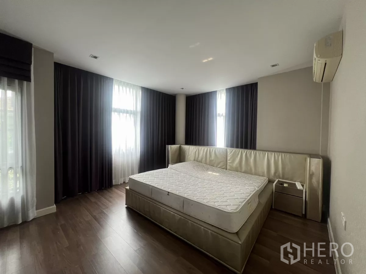 Detached House for sale in Bang Kapi, Bangkok - Master bedroom with upholstered bed frame, dark blackout curtains, and wood floor.
