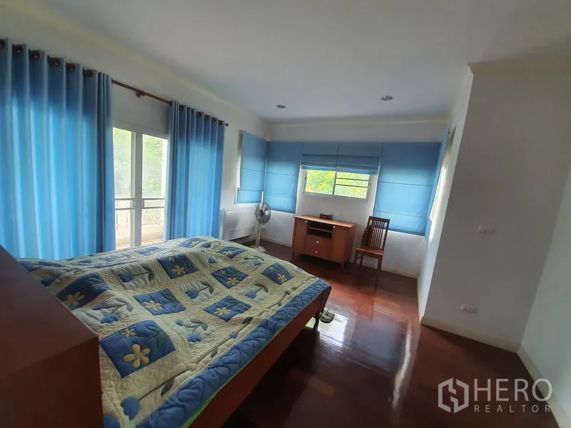 独立式住宅 出租在Lat Krabang, Bangkok - 宽敞主卧，蓝色窗帘，带阳台出入口与抛光木地板。