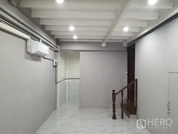 Shophouse for rent in Phra Khanong, Bangkok - Ground-floor interior with white ceiling beams, LED lights, air conditioner, and a small wooden staircase.
