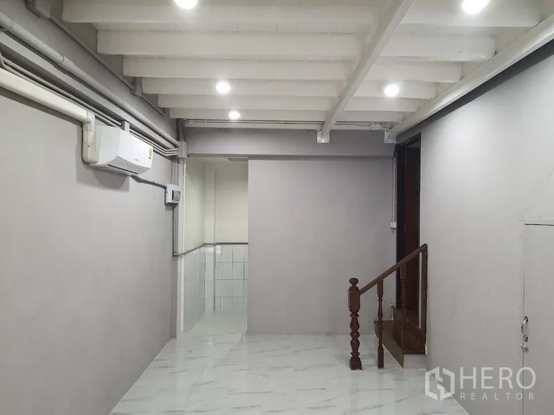 Shophouse for rent in Phra Khanong, Bangkok - Ground-floor interior with white ceiling beams, LED lights, air conditioner, and a small wooden staircase.