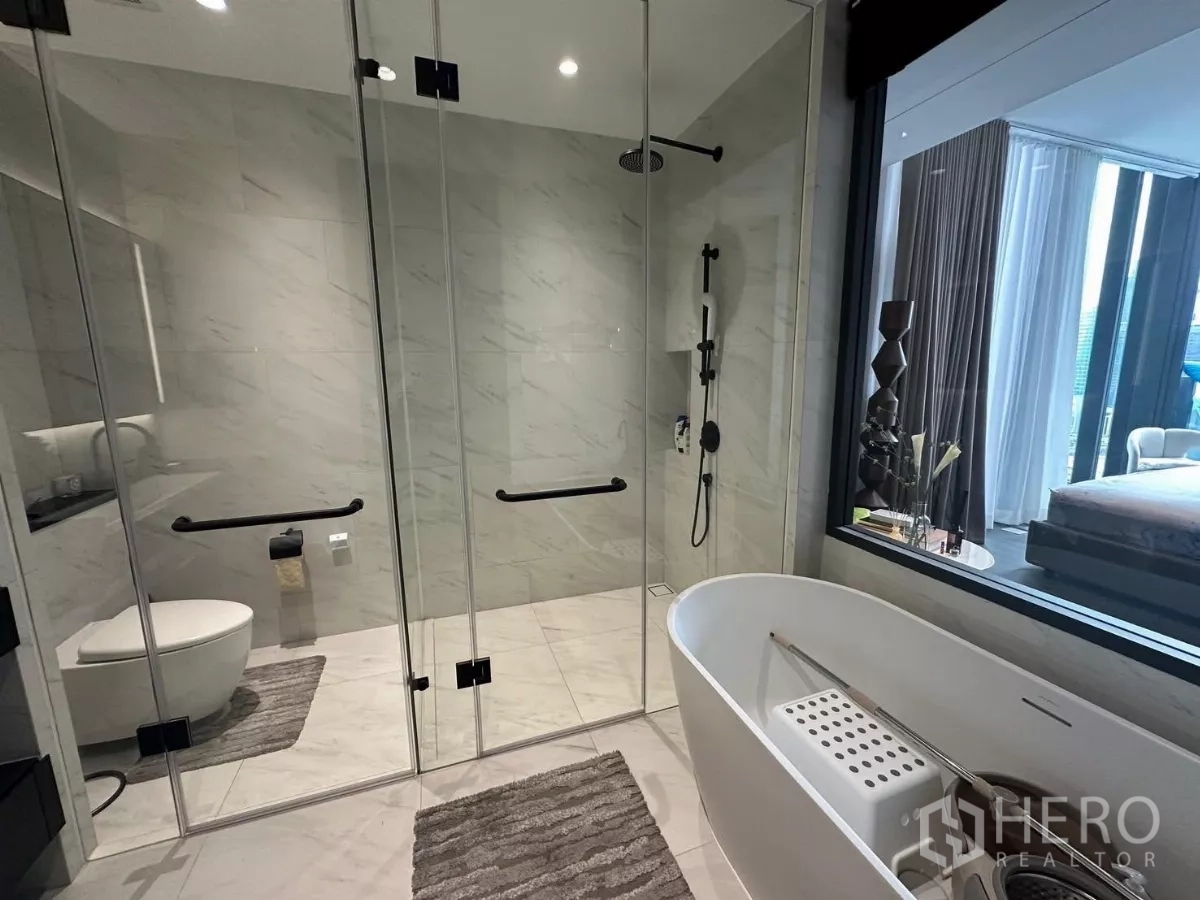 Condominium for rent in Bang Rak, Bangkok - Modern ensuite bathroom featuring a freestanding tub, rain shower, glass partitions, and marble-look tiles.