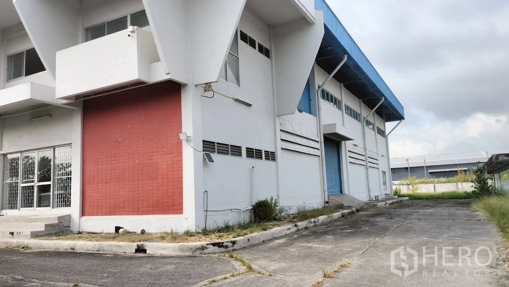 โรงงาน for rent in Lat Krabang, Bangkok - อาคารโรงงานสีขาวผนังแต่งสีแดง พร้อมทางลาดและถนนกว้างด้านข้าง.