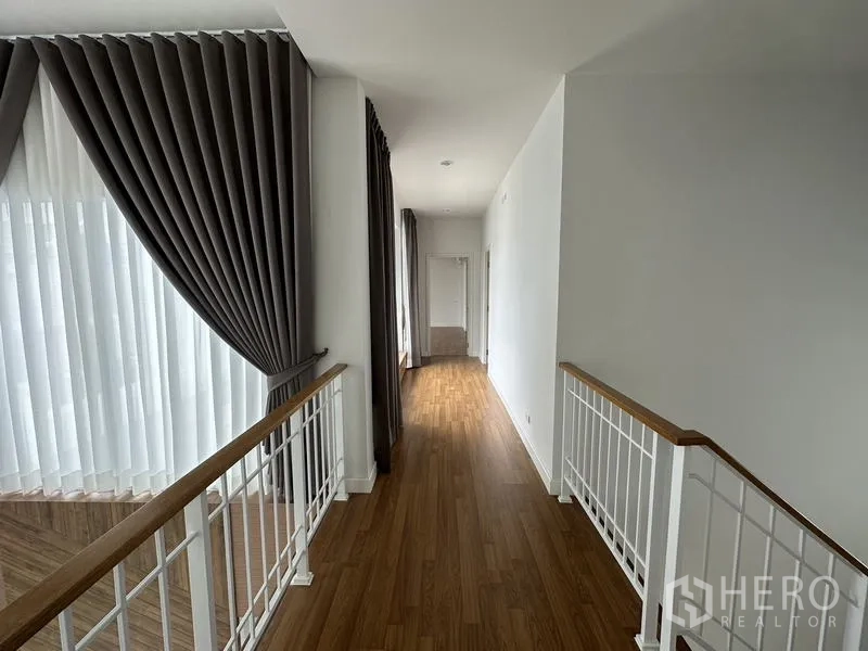 Detached House for sale in Lam Luk Ka, Pathum Thani - Upstairs corridor with white balustrade and wood flooring.
