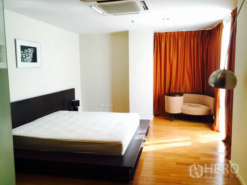 Condominium for rent in Bang Rak, Bangkok - Sunlit master bedroom with wood floors, corner seating and full-length curtains.