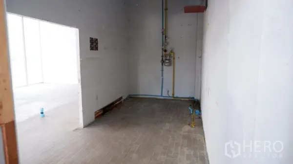 Retail Space for rent in Watthana, Bangkok - Back-of-house utility zone with white walls, exposed plumbing lines, and doorway to the main retail space.