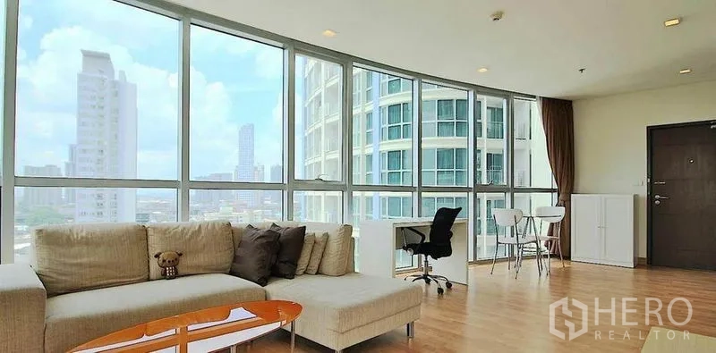 คอนโด ให้เช่าในWatthana, Bangkok - ห้องนั่งเล่นมุมอาคาร กระจกพาโนรามา โซฟา L‑shape โต๊ะทำงาน วิวสกายไลน์ ใกล้ BTS พระโขนง